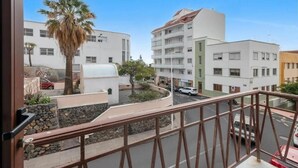 Ein Balkon mit Blick auf eine Straße, Palmen und mehrstöckige Gebäude.
