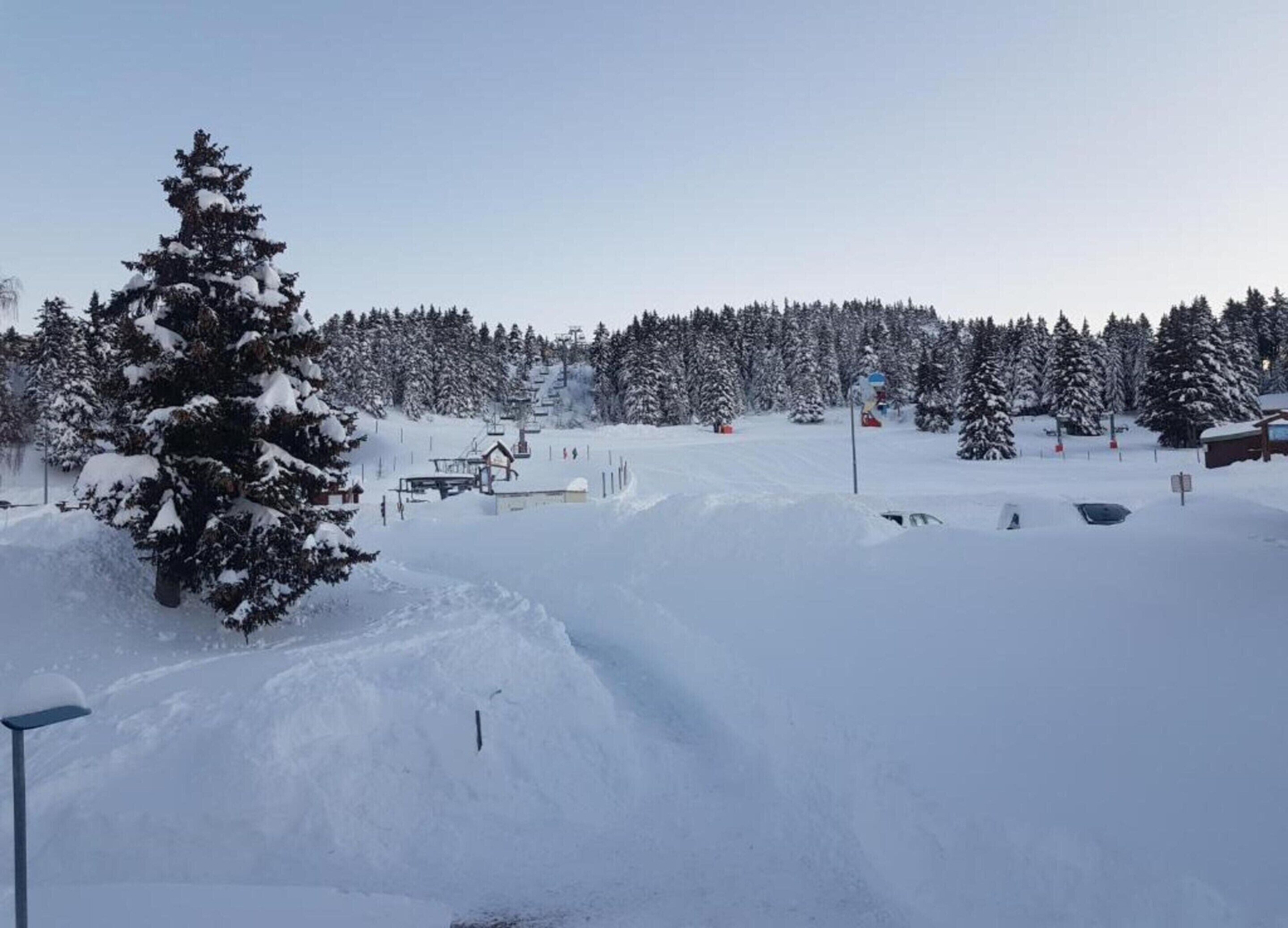 Schneebedeckte Landschaft mit einer Seilbahn, Bäumen und einer Berghütte.
