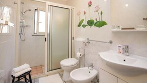 A bathroom with a glass shower enclosure, a toilet, a bidet, and a sink with a mirror.