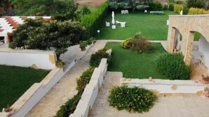 A landscaped garden with a lawn, white chairs, and a stone pathway.