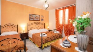 A hotel room with two single beds, a wooden nightstand, a bedside table with a lamp, a vase with flowers, and a painting on the wall.