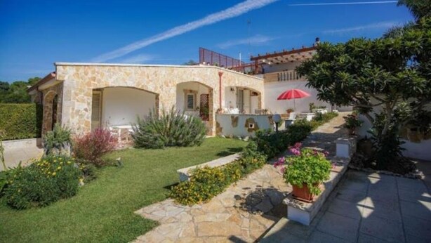 A stone house with a garden, a red umbrella, and a clear blue sky.