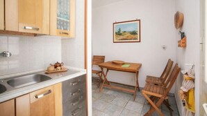 A kitchen with wooden cabinets and a sink, a dining table with chairs, and a painting on the wall.
