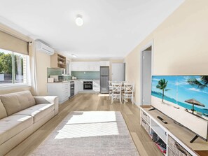 Un appartement moderne comprenant un salon, une cuisine, un coin repas et un téléviseur diffusant une scène de plage.
