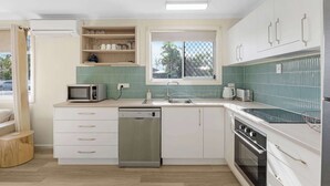 Una cocina compacta con lavavajillas, microondas y estufa. Tiene una ventana con vistas a palmeras y un salpicadero de azulejos verdes.