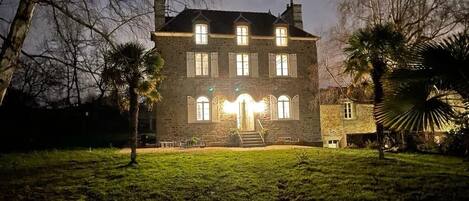A stone building with multiple windows and a central entrance, surrounded by a grassy lawn and palm trees.