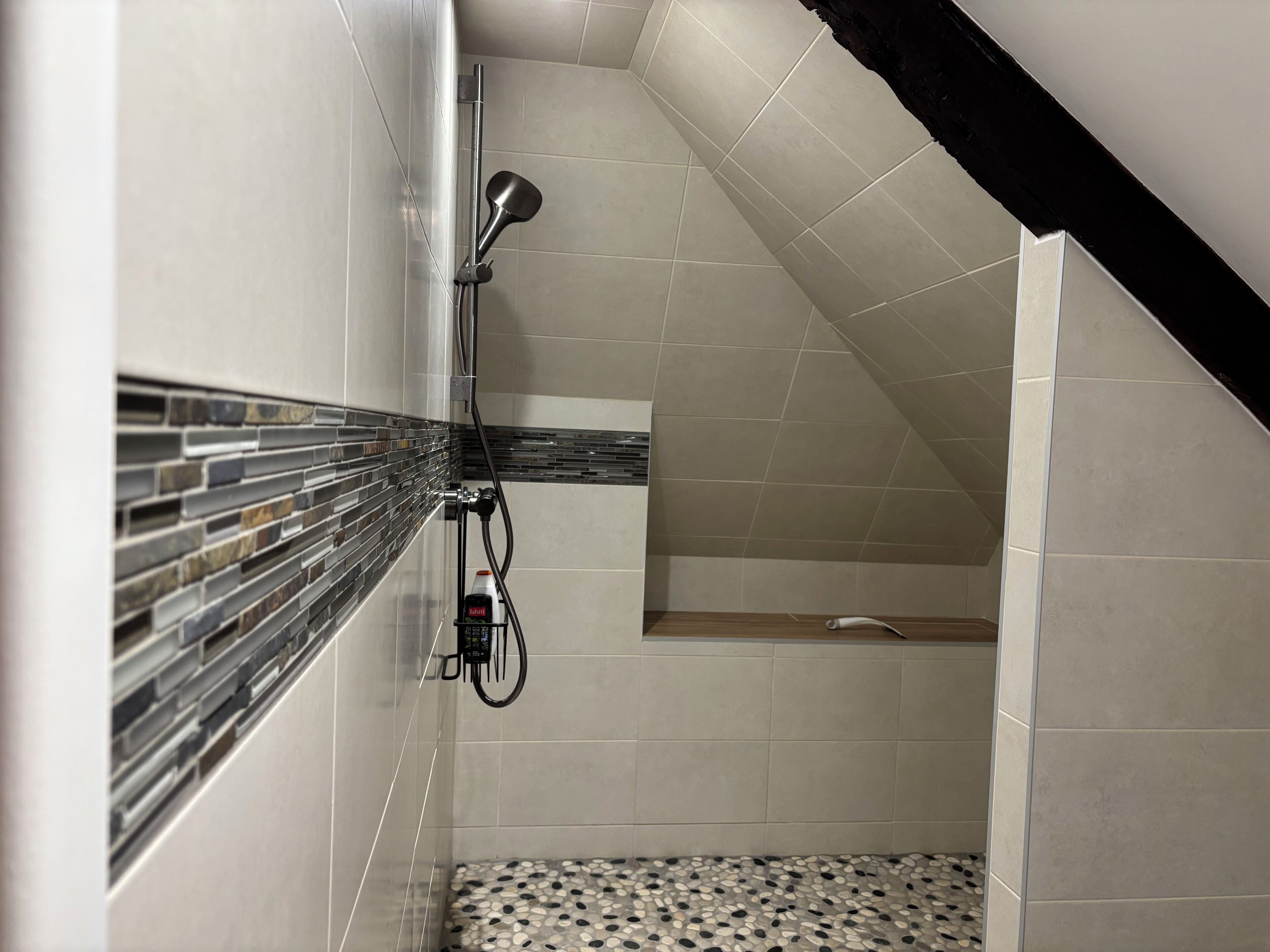 A shower area with a tiled wall, a handheld showerhead, and a tiled floor.