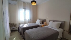 A hotel room with two beds, a chair, a lamp, and a window with curtains. - Villa Yakinthi (CORFU)