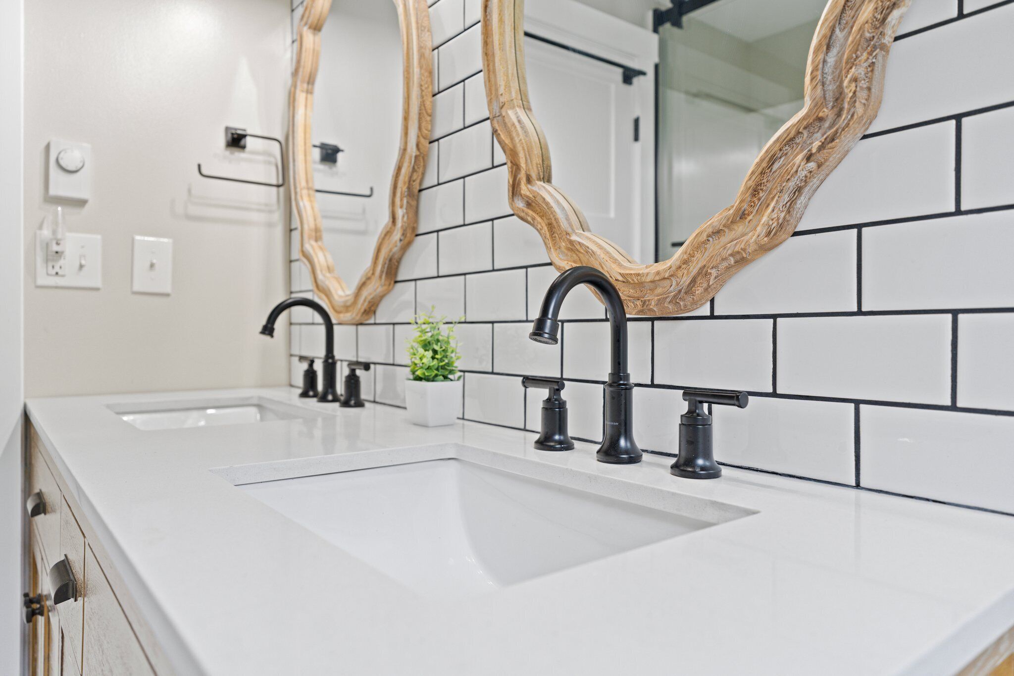 Une salle de bain avec deux lavabos, des robinets noirs et un miroir avec un cadre en bois.