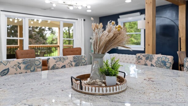 A dining area with a marble table, a decorative tray with a vase and plants, and patterned sofas.