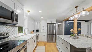 A modern kitchen with stainless steel appliances, white cabinetry, and a marble countertop.