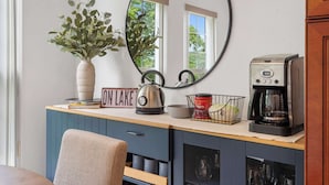 Una cocina con tetera, cafetera y un florero con plantas verdes.