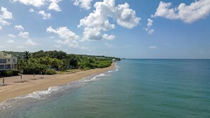Ein Strand mit klarem, blauem Wasser, einem sandigen Ufer und einer Reihe von Strandsonnenschirmen.