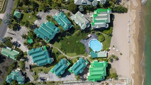 Luftaufnahme eines Resorts mit mehreren Gebäuden, einem Swimmingpool und einem Strand.
