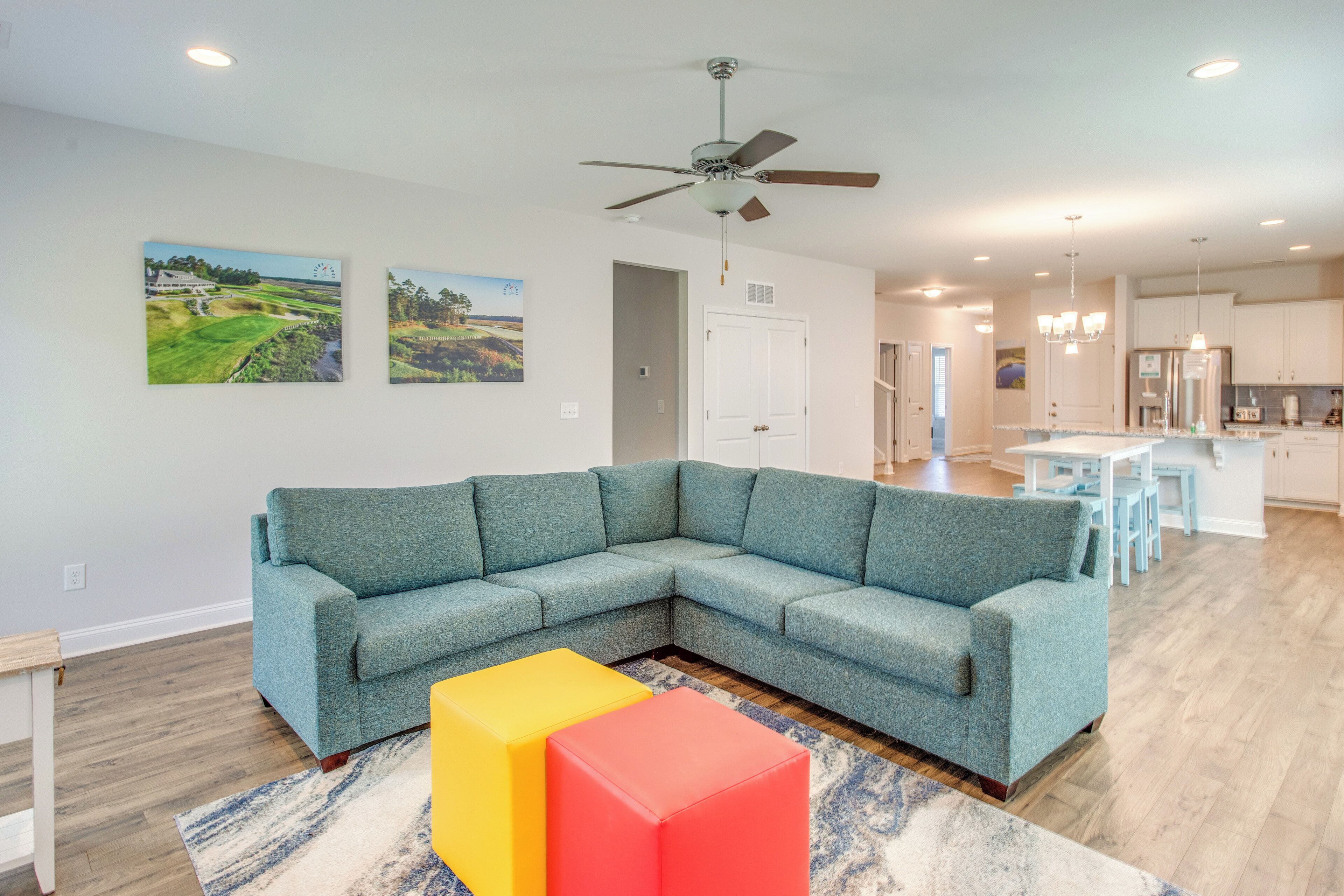 A modern living room with a sectional sofa, a ceiling fan, and artwork on the walls.
