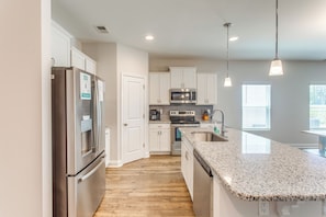 A modern kitchen with stainless steel appliances, white cabinetry, and a granite countertop. - 4 Mi to Beaches: Sleek Retreat in Ocean Isle Beach (Ocean Isle Beach)