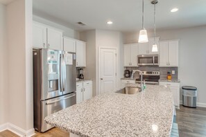 A modern kitchen with white cabinetry, stainless steel appliances, granite countertops, and pendant lighting. - 4 Mi to Beaches: Sleek Retreat in Ocean Isle Beach (Ocean Isle Beach)
