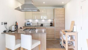 A modern kitchen with a central island, stainless steel appliances, and wooden cabinetry. - GuestReady - Spacious 1BR in East London w Balcony (London)