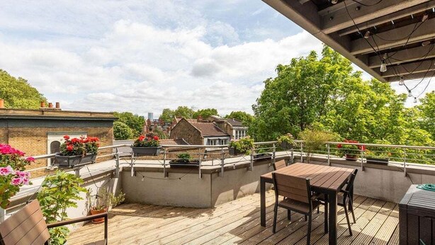 A wooden deck with a table and chairs, surrounded by potted plants and flowers. - GuestReady - Spacious 1BR in East London w Balcony (London)