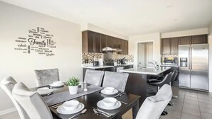 Una cocina moderna con armarios oscuros, un refrigerador de acero inoxidable y un comedor con mesa puesta para cuatro.