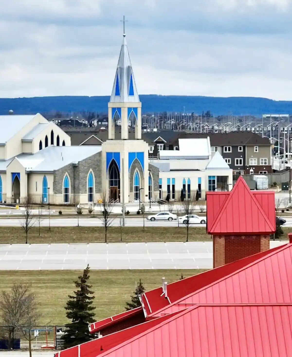 A church with a prominent steeple and blue accents, surrounded by residential buildings and a clear sky.