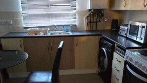 Een kleine keuken met een wasmachine, magnetron en een eethoek met een stoel.