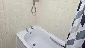 Een badkamer met een wit bad, een douchekop en een handdoekhouder.
