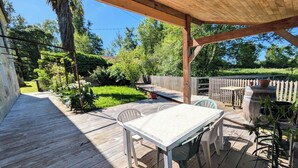 A covered wooden deck with a table and chairs, surrounded by a wooden fence and greenery. - Waterfront house - Nature, relaxation & family (Sainte-Marthe)