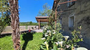 A garden with a palm tree and white flowers, a wooden pergola, and a rustic building with a balcony. - Waterfront house - Nature, relaxation & family (Sainte-Marthe)