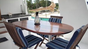A round wooden table with four striped chairs, a vase, and a view of boats and trees.
