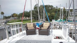 A deck with two wicker chairs and a table, overlooking a marina with multiple boats.