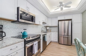 A modern kitchen with white cabinetry, a stainless steel refrigerator, a microwave, a stove, and a ceiling fan. - Island Reef 703 (Fort Myers Beach)