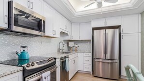 Une cuisine moderne avec des meubles blancs, un réfrigérateur en acier inoxydable, un four à micro-ondes encastré et une cuisinière à gaz.