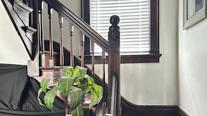 A wooden staircase with a handrail, a window with blinds, and a potted plant.