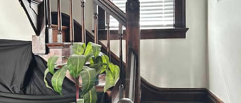 Un escalier en bois avec une rampe, une fenêtre avec des stores et une plante en pot.