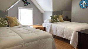 A bedroom with two beds, a wooden floor, a window, and a door.