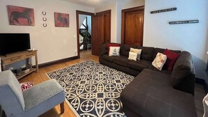 A living room with a ceiling fan, a TV on a wooden stand, a patterned rug, two sofas, and a staircase leading to an upper floor.