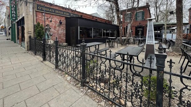 A brick building with a sign reading "O'Shea's Irish Pub" and outdoor seating with tables and chairs.