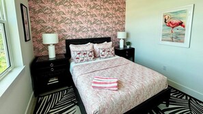 A bedroom with a bed, two bedside tables, a window, and a wall with a flamingo painting.