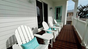 Eine Veranda mit weißen Adirondack-Stühlen, einem türkisfarbenen Kissen, einer Tür und einem Geländer.