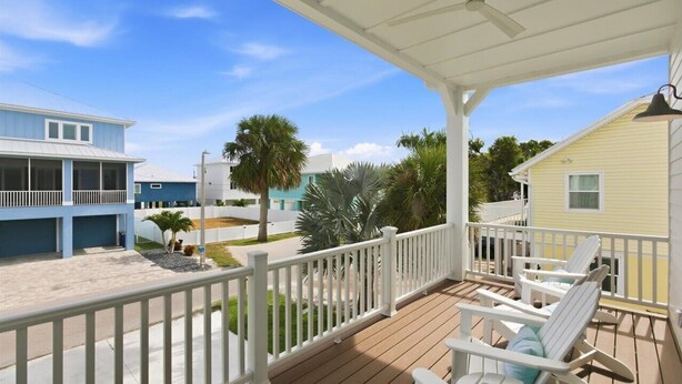 A wooden deck with white railings, a covered area with chairs, and a view of neighboring buildings. - Ocean Pearl - Steps from the Beach (Fort Myers Beach)