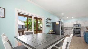 A modern kitchen with white cabinets, a large dining table, and a view through the glass door. - Sandy Toes Bungalow: Dog-Friendly with Private Pool (Oak Island)