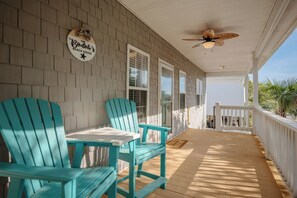 A covered porch with two turquoise Adirondack chairs, a ceiling fan, and a sign reading 'The Bodah's Beach House.'