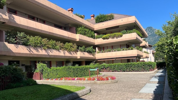 Un hôtel à plusieurs étages doté de balcons, d’une cour dallée et entouré de verdure.