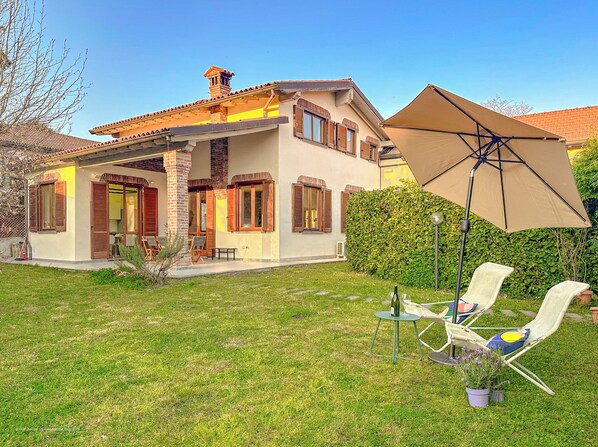 A two-story house with a patio area, outdoor seating, and a large umbrella. - Villa Corelli - Parking and Exclusive garden (Milan)
