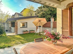 A patio with a wooden table and chairs, a lawn, and a house with a brick facade and a window. - Villa Corelli - Parking and Exclusive garden (Milan)
