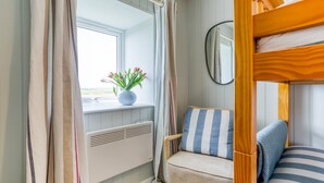 A cozy cabin interior with a window, a radiator, a chair with striped cushions, and a bunk bed. - Bryntirion Wyn - sleeps 4 guests  in 2 bedrooms (Aberffraw)