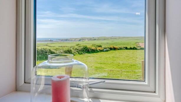 A window with a clear view of a grassy field and distant hills. - Bryntirion Wyn - sleeps 4 guests  in 2 bedrooms (Aberffraw)