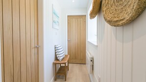 A narrow hallway with wooden doors, a bench with a striped cushion, and a woven basket hanging on the wall. - Bryntirion Wyn - sleeps 4 guests  in 2 bedrooms (Aberffraw)