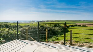 A paved walkway leading to a fenced area with a view of a coastal landscape. - Bryntirion Wyn - sleeps 4 guests  in 2 bedrooms (Aberffraw)